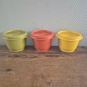 Może przedstawiać: Trzy pojemniki do przechowywania żywności z tworzywa sztucznego w kolorach zielonym, pomarańczowym i żółtym. Każdy pojemnik ma pasującą pokrywkę z wzorem promieni słonecznych. Pojemniki stoją na drewnianej powierzchni.