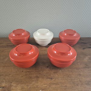 Op de afbeelding: Zes stapelbare kommen, vier zijn rood en twee zijn wit. De kommen zijn gemaakt van plastic en hebben een gladde, ronde vorm.
