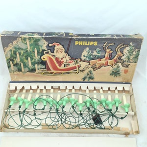 Op de afbeelding: Een vintage doos met Philips kerstverlichting met een groene draad en witte lampjes. De doos heeft een feestelijke illustratie van Sinterklaas in een slee die door rendieren wordt getrokken.