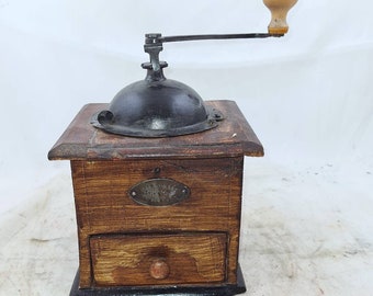 Op de afbeelding: Antiek houten koffiemolen met een zwarte metalen molen en een houten kruk. De molen heeft een lade om de gemalen koffie op te vangen en een metalen plaatje met de tekst "ALFRED  MAURER  PARIS".