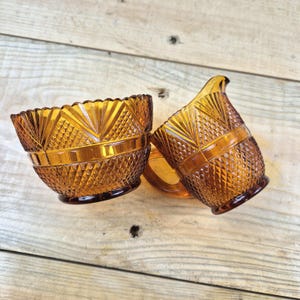 Op de afbeelding: Een set van twee suiker- en roompotten van amberkleurig glas met een diamantpatroon. De potten hebben een gegolfde rand en een reliëfdesign.