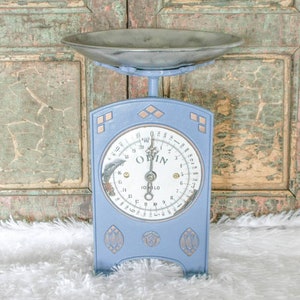 Puede incluir: Una báscula de cocina vintage azul con una cara blanca y detalles dorados. La báscula tiene un cuenco redondo de metal y lee "10 KILO" y "OBIN".