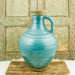 Può includere: Un grande vaso in ceramica blu turchese con un'ampia apertura e un manico. Il vaso ha una finitura testurizzata e smaltata e una forma arrotondata.