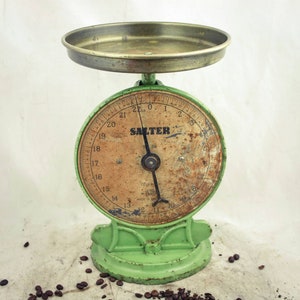 Puede incluir: Una báscula de cocina vintage verde Salter con una parte superior de latón y una cara redonda con marcas negras. La báscula está marcada con números del 13 al 22 y la palabra "Salter" en letras negras.