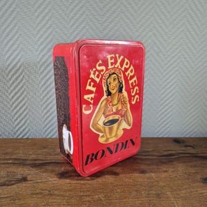 Könnte beinhalten: Rote Metalldose mit einer Frau in einem Blumenkranz, die eine Tasse Kaffee hält. Die Dose trägt die Aufschrift "Cafés Express Bondin" in schwarzer Schrift.