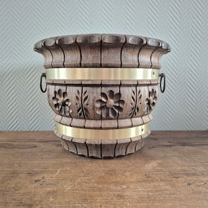 Peut inclure: Un pot en bois avec une bordure en laiton et des détails floraux sculptés. Le pot a deux poignées en laiton sur les côtés.