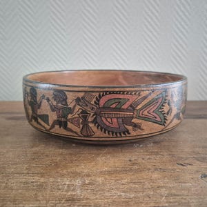 以下が含まれることがあります： 黒、緑、ピンク、白で描かれた、スタイリッシュな人物と幾何学模様のペイントが施された茶色の陶器のボウルです。