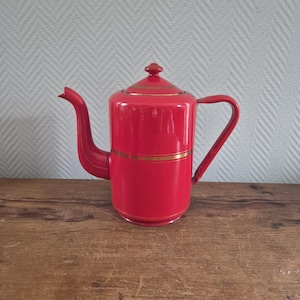 Op de afbeelding: Een rode emaille theepot met een gouden rand. De theepot heeft een deksel en een handvat.