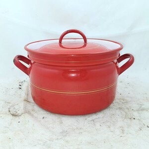 Op de afbeelding: Rode emaille pan met een deksel en twee handvatten. De pan heeft een gouden rand in het midden.