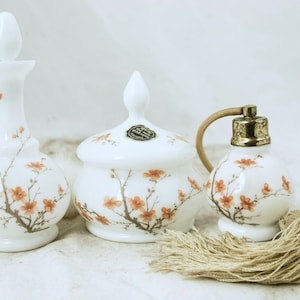 Pode incluir: Um conjunto de frascos de perfume de porcelana branca com um design floral. O conjunto inclui uma garrafa com rolha, um frasco com tampa e um pequeno frasco atomizador com um tassel.