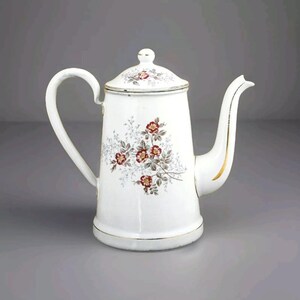 Puede incluir: Cafetera de esmalte blanco con un diseño floral en tonos rojos y marrones. La cafetera tiene un borde dorado alrededor del pico y una tapa con un diseño floral.