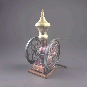 Può includere: Macinacaffè antico con parte superiore e terminale in ottone, corpo bordeaux e due grandi ruote a raggi. Il macinacaffè ha un piccolo cassetto in legno ed è montato su una base di legno. Le ruote hanno un diametro di circa 25 cm.