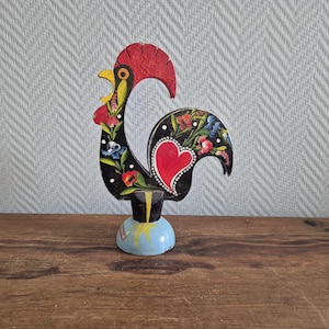 Peut inclure: Une figurine de coq en bois noir et rouge avec une base bleue. Le coq est peint avec des fleurs colorées et un cœur rouge sur ses plumes de la queue.