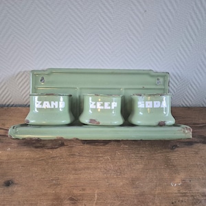 May include: A vintage green enamel wall-mounted shelf with three containers labeled "ZAND", "ZEEP", and "SODA".