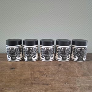 Op de afbeelding: Set van vijf zwarte en witte keramische kruidenpotten met een bloemenmotief. Elke pot heeft een zwart deksel.