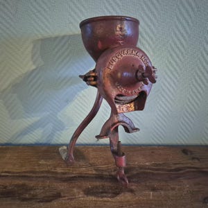 May include: A vintage Husqvarna No. 2 coffee grinder in a rustic red hue. The cast iron grinder features a hopper, a crank, and a clamp for securing it to a surface. The words "HUSQVARNA NO. 2" and "MADE IN SWEDEN" are embossed on the grinder.