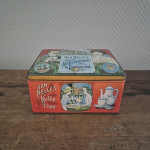 Op de afbeelding: Vintage blikken doos met een rood, oranje en geel ontwerp. De doos heeft een illustratie van een winkel met de tekst "Van Nelle's Stoom Koffiebranderij en Theehandel" en "Van Nelle's Koffie Thee".