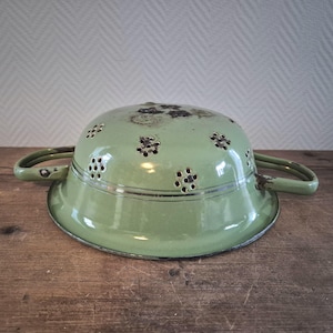 May include: A vintage green enamel colander with a gold rim and a floral pattern. The colander has two handles and is made of metal.