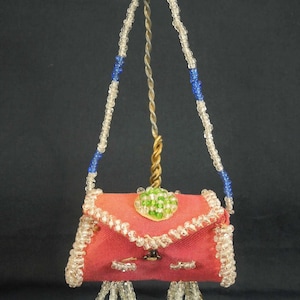 May include: A pink beaded purse with a green beaded flower on the front. The purse has a beaded strap with blue beads.