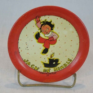 May include: Red and white metal plate with a cartoon illustration of a child jumping over a candle. The plate has a red rim and a white center with red polka dots. The text "Jack Be Nimble" is written in black around the edge of the plate.