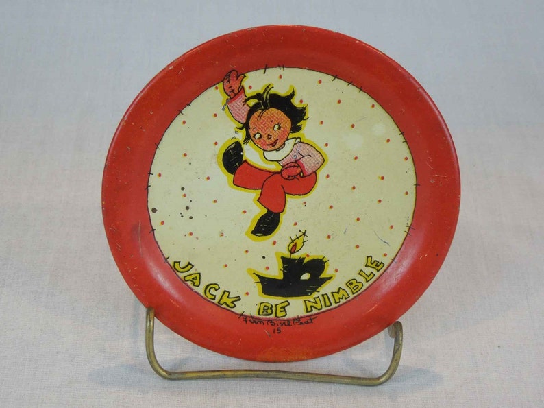 May include: Red and white metal plate with a cartoon illustration of a child jumping over a candle. The plate has a red rim and a white center with red polka dots. The text "Jack Be Nimble" is written in black around the edge of the plate.