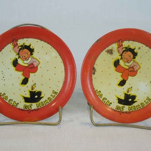 May include: Two red metal plates with a white center and a black and white illustration of a child jumping over a candle. The plates have the text "Jack Be Nimble" printed on them.