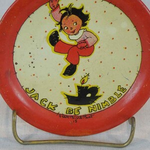 May include: A red and white metal plate with a cartoon image of a girl jumping over a candle. The plate has the text "Jack Be Nimble" around the edge and "Fun &  Fizzle Fact 15" at the bottom.