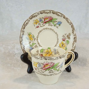 May include: A vintage teacup and saucer set with a floral pattern in shades of yellow, pink, blue, and green. The cup and saucer are white with a gold trim.