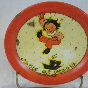 May include: A red and white metal plate with a cartoon illustration of a girl jumping over a black cat. The plate has a white background with red polka dots and the text "Jack Be Nimble" in black lettering. The text "Fun 15&cent;  Post 15" is also printed on the plate.