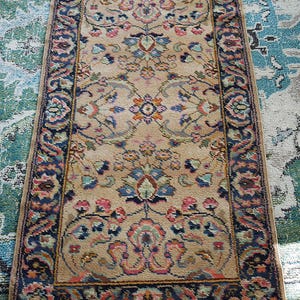 May include: A vintage rug with a floral pattern in shades of pink, blue, and green. The rug has a dark blue border with intricate designs. The rug is beige in color and has a fringed edge.