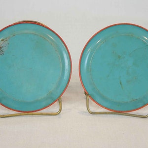 May include: Two turquoise blue metal coasters with a red rim. The coasters are on a gold metal stand.