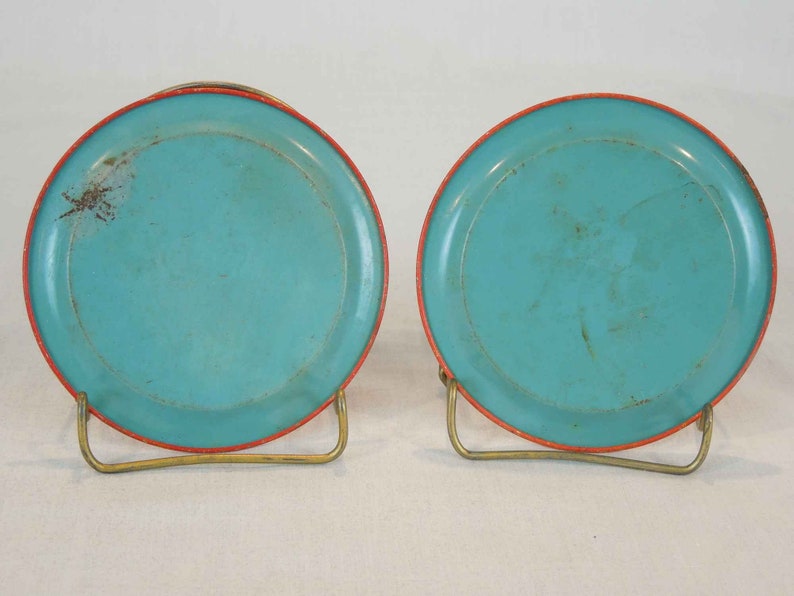 May include: Two turquoise blue metal coasters with a red rim. The coasters are on a gold metal stand.
