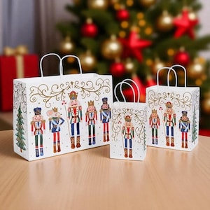 May include: Three white gift bags with handles, featuring a Nutcracker soldier design in red, blue, and gold. The bags are arranged on a wooden surface, with a Christmas tree and decorations in the background.