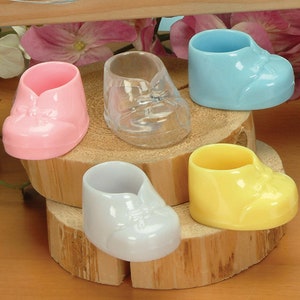 Pu&ograve; includere: Cinque contenitori a forma di scarpa da bambino in rosa, blu, trasparente, bianco e giallo. I contenitori sono in plastica e hanno una piccola apertura nella parte superiore.