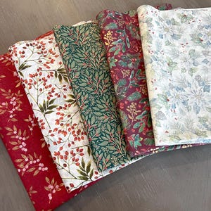 May include: Five folded pieces of fabric featuring holiday-themed patterns. The designs include red fabric with pink berries, white fabric with red berries, dark green fabric with leaves, deep red fabric with pine branches, and white fabric with poinsettias.