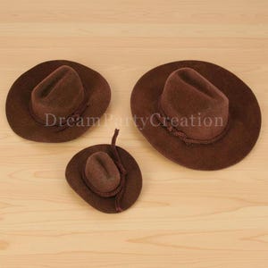 May include: Three brown cowboy hats of varying sizes are arranged on a light wood surface. The hats have a classic design with a rounded crown and a wide brim. The text "Dream Party Creation" is visible on the hats.