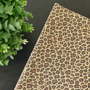 May include: A notebook with a tan leopard print pattern. The cover features brown and black spots on a tan background. A green plant with small white flowers is in the upper left corner.