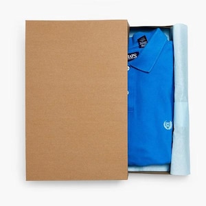 May include: A bright blue polo shirt with a collar and a white embroidered logo on the chest, partially covered by a brown cardboard box lid. The shirt features a button placket and is nestled inside a box lined with light blue tissue paper.