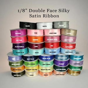 May include: A collection of 1/8 inch double face silky satin ribbon spools in a wide variety of colors including black, white, silver, pink, red, blue, green, and yellow. Each spool is labeled with its specific color name in white text.