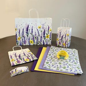 May include: A collection of lavender-themed gift packaging. Includes white paper gift bags, wrapping paper, and tags, all decorated with watercolor-style lavender and yellow flower designs. Also includes purple and yellow paper sheets and yellow ribbon.