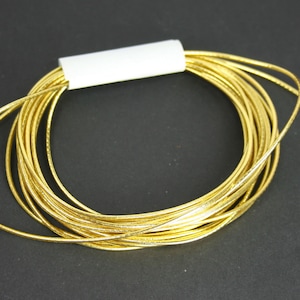 May include: A spool of gold metallic cord, wound in a circle, with a white label on the spool.