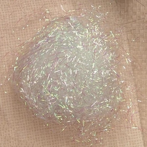 May include: A ball of iridescent, white, and light purple tinsel. The tinsel is tightly wound, creating a dense, fluffy texture. The light reflects off the strands, creating a shimmering effect. This decorative tinsel is suitable for crafts and holiday decorations.
