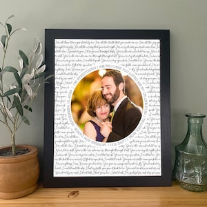 May include: A black framed print with a white background and black text. The text is a song lyric from Celine Dion's song "Because You Loved Me". A circular photo of a woman and a man is in the center of the print. The photo is surrounded by the song lyrics.
