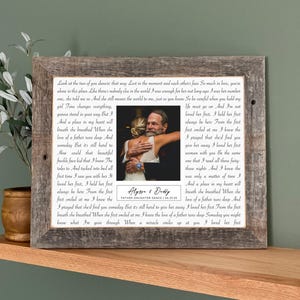 May include: A framed photo print with a rustic wooden frame. The print features a black and white photo of a father and daughter embracing, with a poem and the text "Alyson & Dolly, Father-Daughter Dance 06.25.25". The frame is displayed on a wooden shelf.
