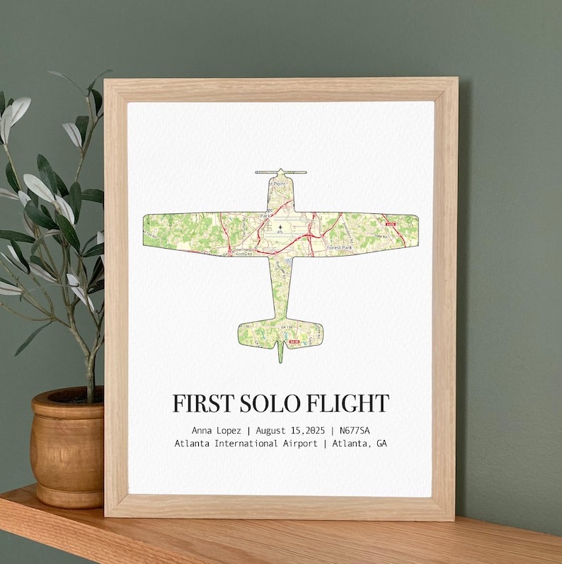 May include: A framed print featuring a green map-style airplane silhouette. The text "FIRST SOLO FLIGHT" is below the image, along with the name Anna Lopez, date, aircraft tail number, and airport location.
