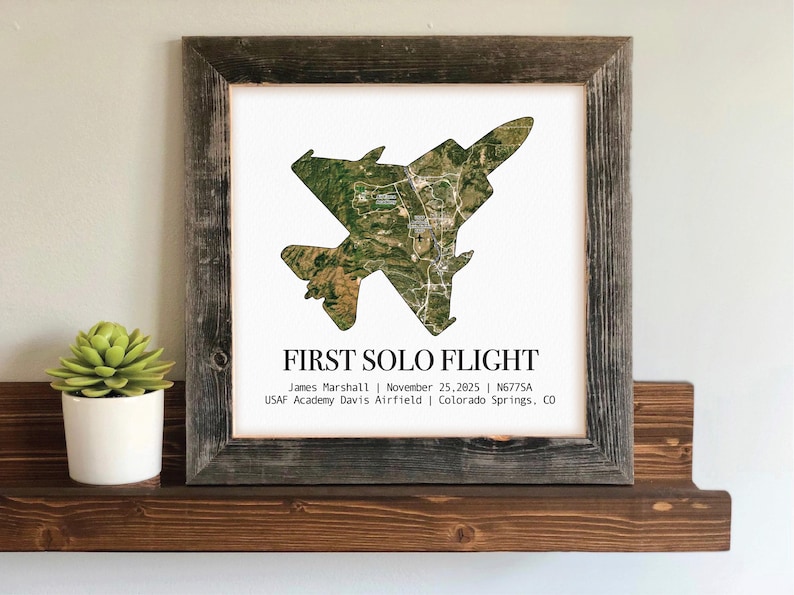 May include: A framed print featuring a detailed aerial view of an aircraft, with the text "FIRST SOLO FLIGHT." The image is set against a white background, framed in rustic wood. Additional text includes a name, date, and location.