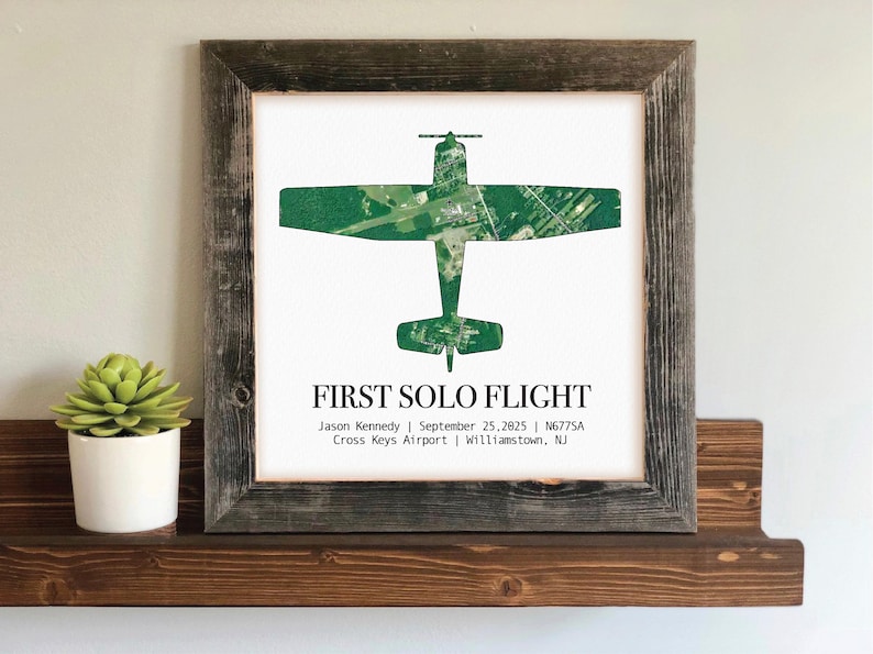 May include: A framed print featuring a green airplane silhouette over a white background. The text "FIRST SOLO FLIGHT" is displayed below the image, along with details about the flight. The frame is made of rustic, weathered wood.