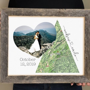Op de afbeelding: Een ingelijst afdruk met een hartvormige foto van een stel op een bergtop, een kaart van het gebied en de tekst "October 12, 2019" en "andrew & emilia".