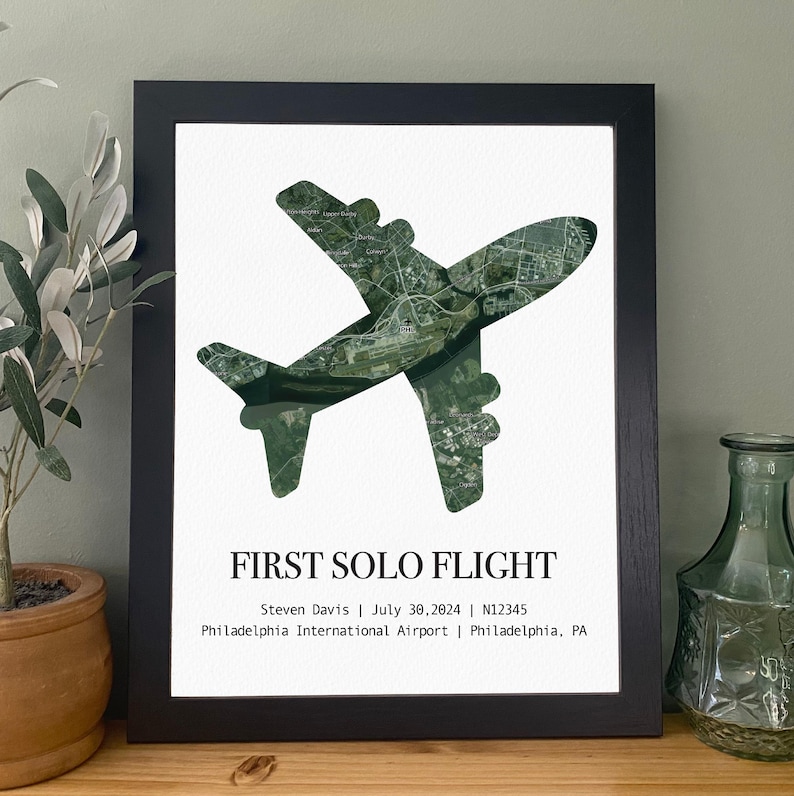 May include: A framed print featuring a green airplane silhouette filled with a detailed aerial view. The text "FIRST SOLO FLIGHT" is displayed below, along with the pilot's name, date, aircraft registration, and airport location.