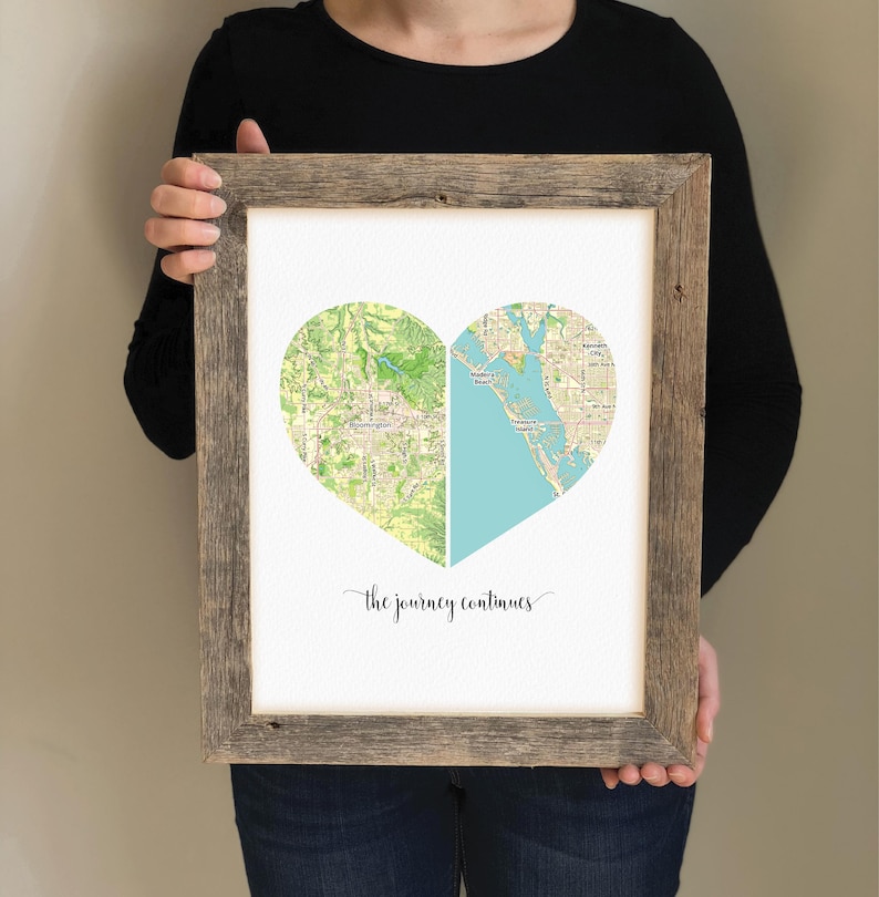 May include: A framed print with a heart-shaped map divided in half. The left side of the heart is a green map of a city, and the right side is a blue map of a coastline. The text "the journey continues" is printed below the heart.